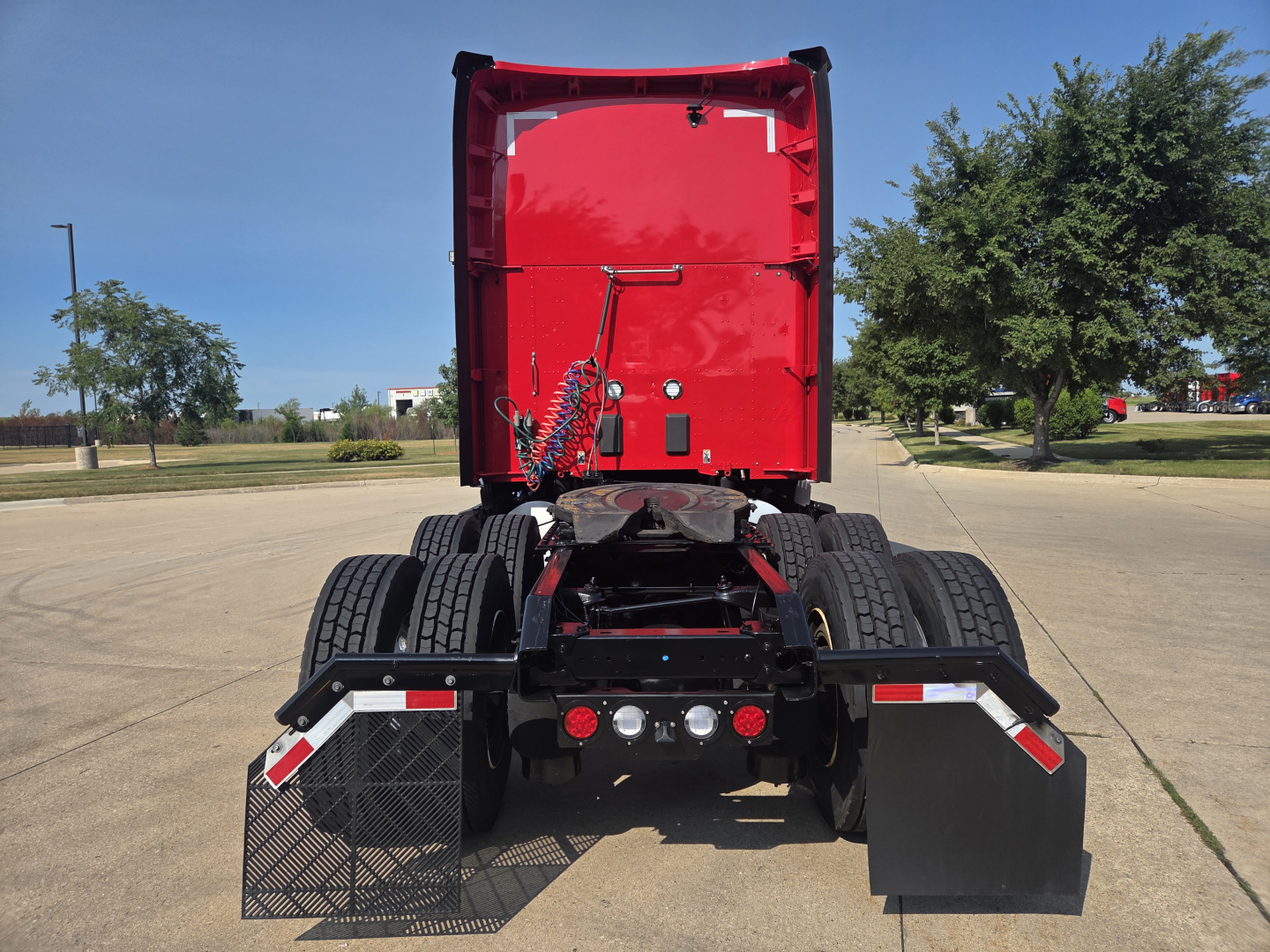 Kenworth truck rear view showing dual rear axles and red cab, with mud flaps and step access.