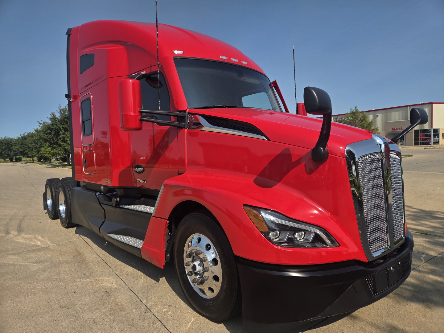 Kenworth T680 tractor cab in red, side angle view with aerodynamic mirrors and chrome grille