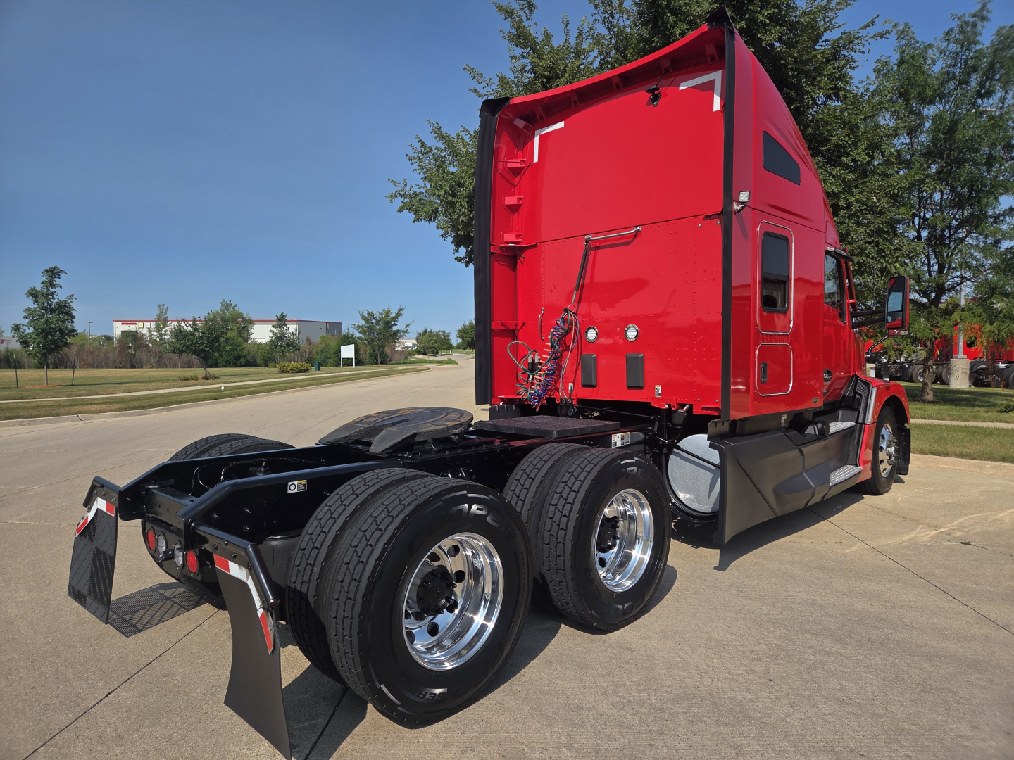 Kenworth T680 sleeper tractor with red cab, dual rear axles, and chrome wheels parked in lot showing rear view and fifth wheel.