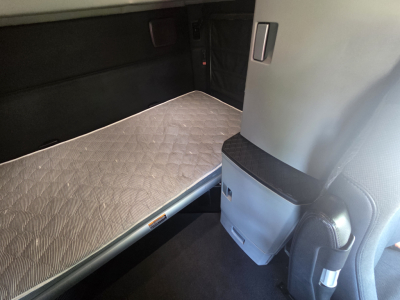 Truck sleeper cab interior showing a bed platform with quilted mattress, side storage cabinet, and cabin wall panel.