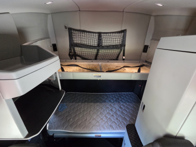 Truck sleeper cab interior with bunk bed setup and storage compartments in a Kenworth T680, view showing upper bunk with netting and lower/cargo area.