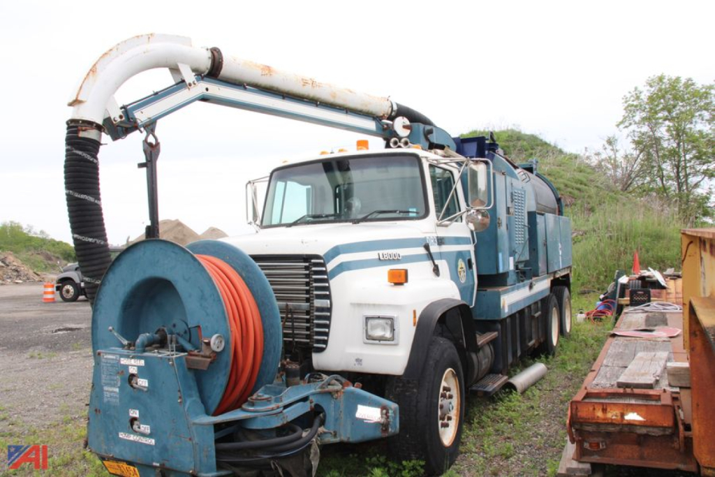 Ford LNT8000 vacuum truck with large hose reel and vac system, white cab with blue body, vacant lot in background.