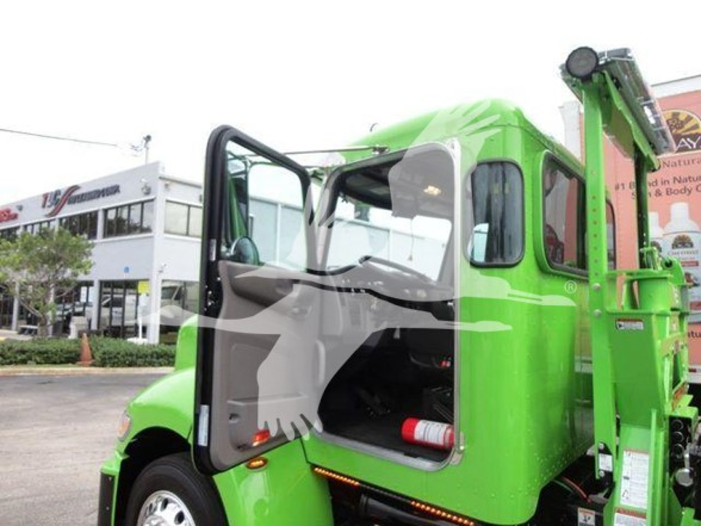 Truck cab open door view showing bright green Peterbilt 337 rollback utility truck with crane arm and interior dashboard visible.