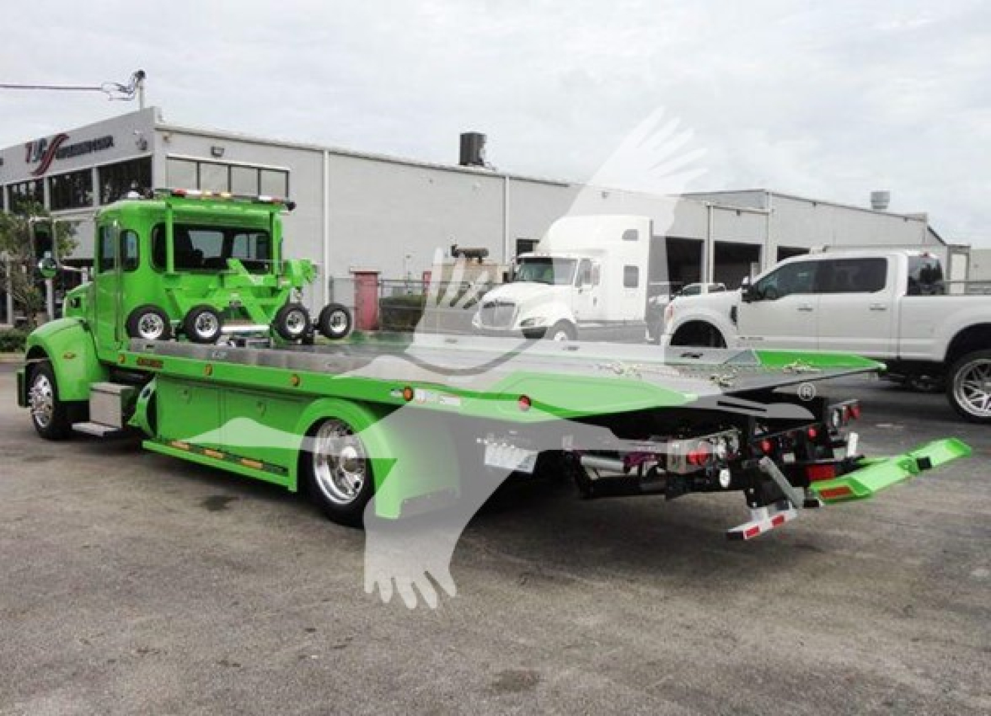 Truck trailer rollback with bright green tow truck and matching green equipment carrier in a lot.