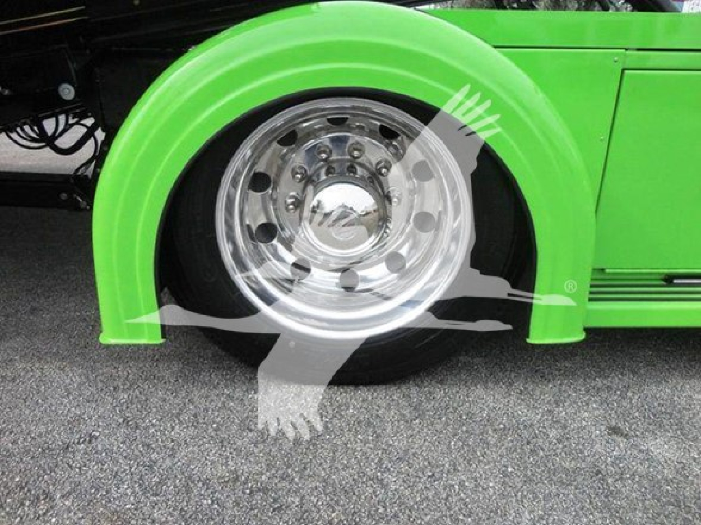 Truck wheel and fender close-up on a green Peterbilt 337 rollback truck showing chrome alloy wheel, green fender, and surrounding asphalt.