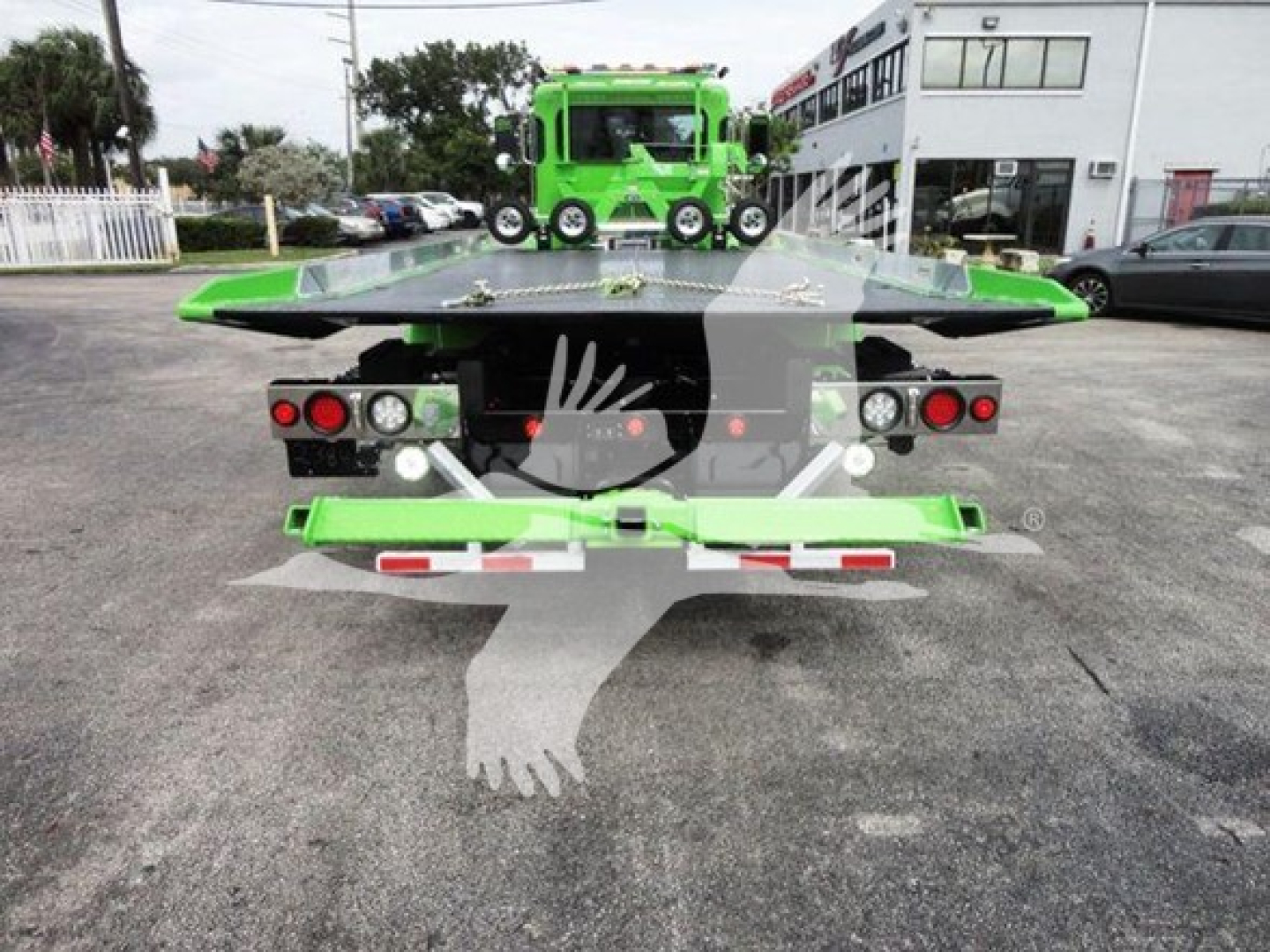 Back view of a green Peterbilt 337 rollback tow truck showing loading bed with red tail lights and rear bumper.
