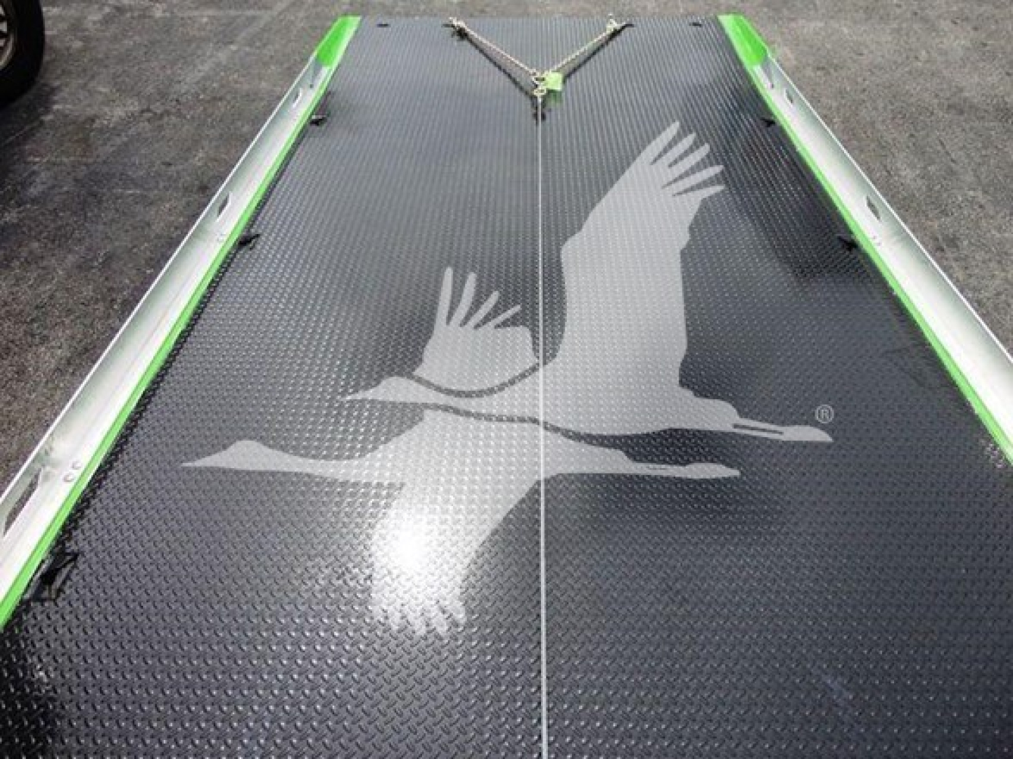 Tractor-trailer rollback bed with a large white bird graphic on black diamond-plate surface and green side rails.