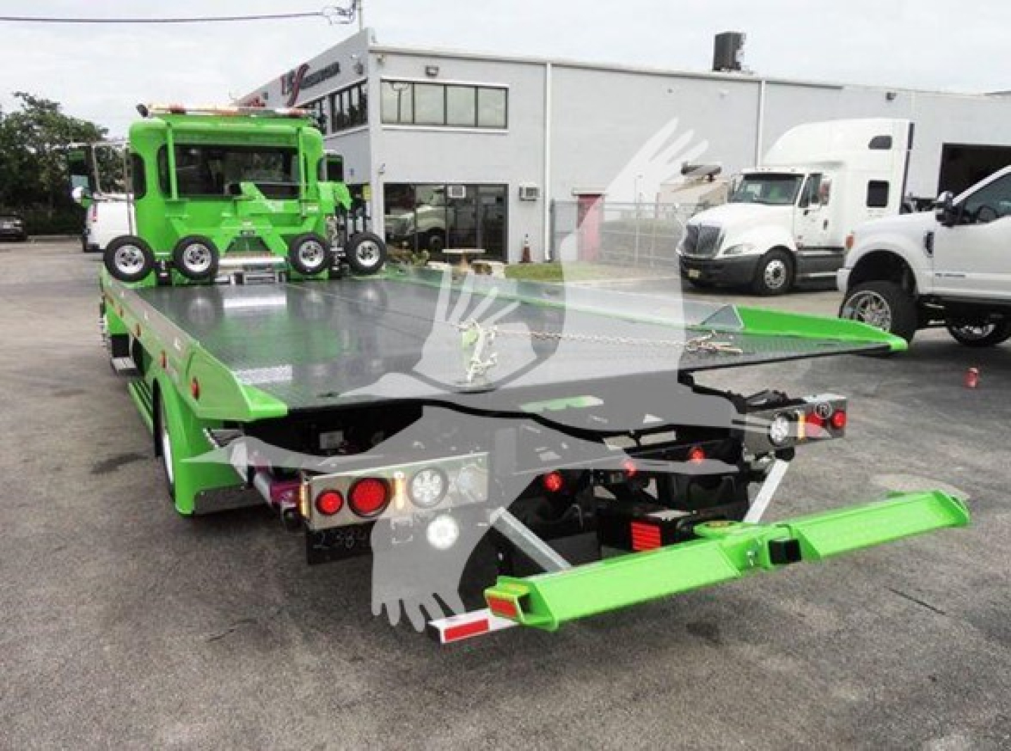 Peterbilt 337 rollback tow truck with bright green flatbed and rear loading ramps, viewed from rear-left in dealership lot.