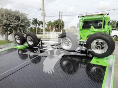 Roll-off tow truck chassis with spare wheels on trailer bed and a bright green Peterbilt 337 cab in background.
