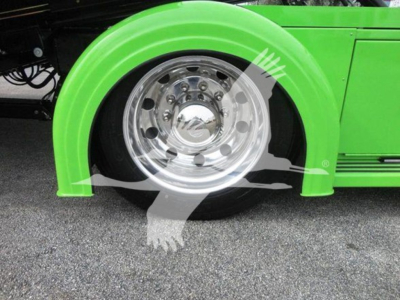 Truck wheel and fender close-up on a green Peterbilt 337 rollback truck showing chrome alloy wheel, green fender, and surrounding asphalt.