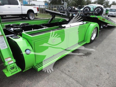 Green Peterbilt rollback truck side view showing flatbed with hydraulic ramps and storage compartments.