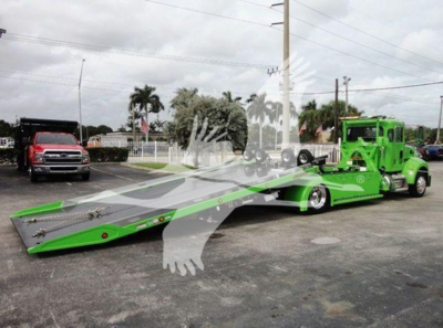 Green Peterbilt rollback tow truck with a long car hauler bed, cab in lime green, and another red truck in background.