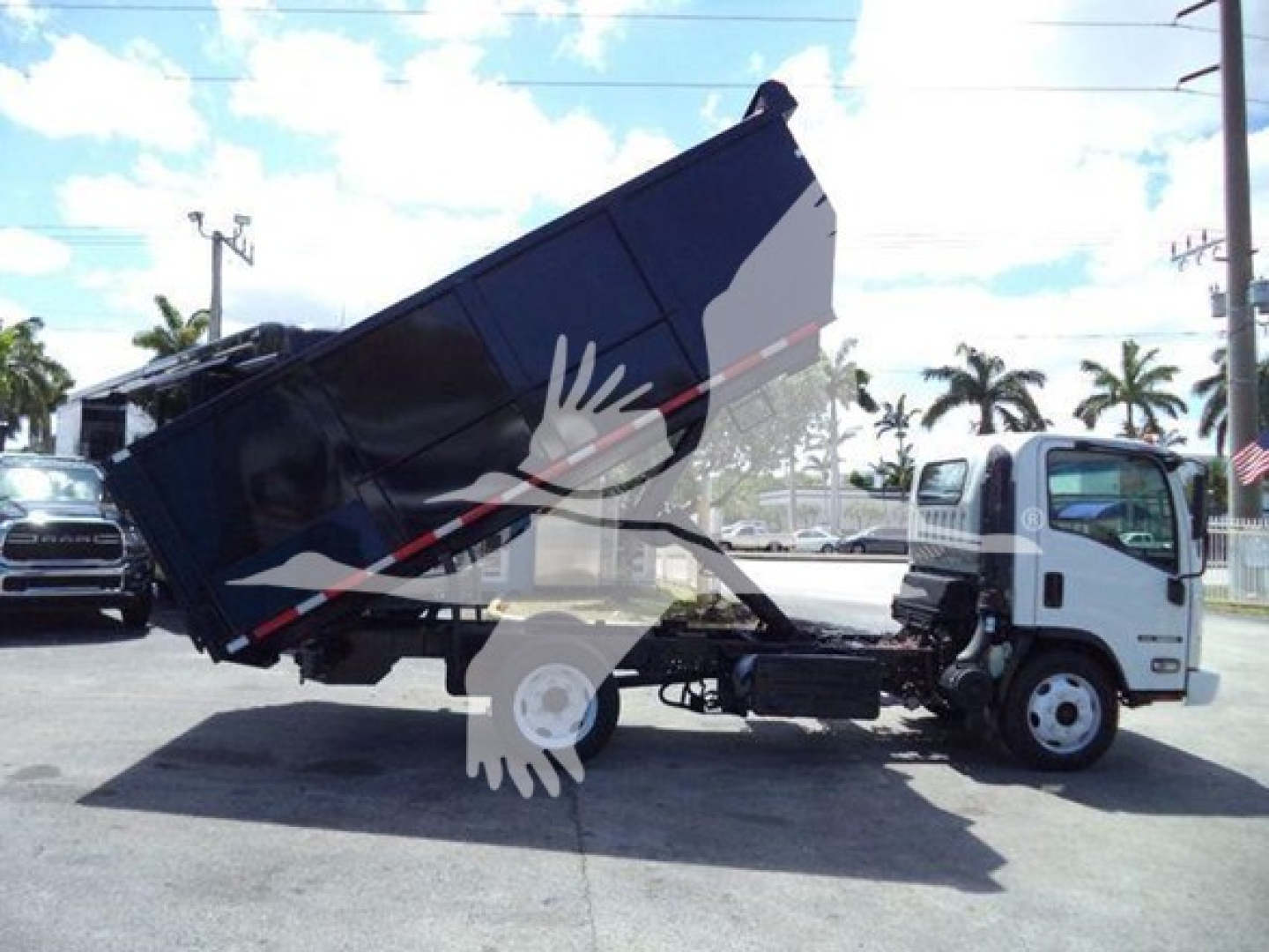 Isuzu NPR/NQR style dump truck with tilted dump bed in service position, white cab, black dump body, visible side profile, clear sky.