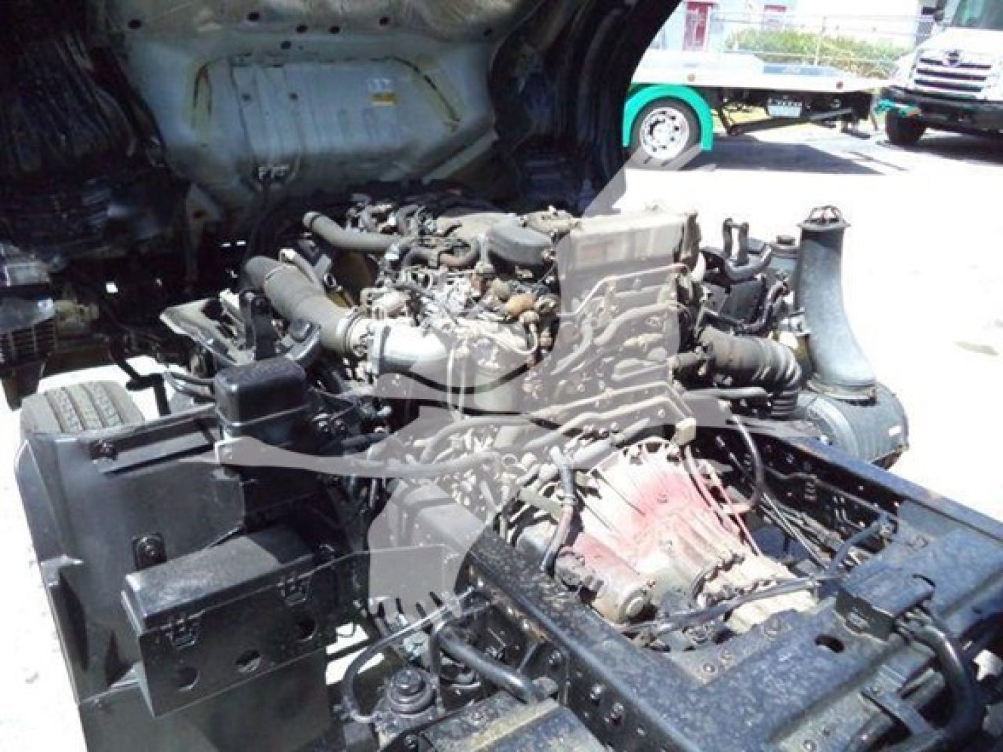 Isuzu truck engine bay visible with exposed engine and components; no readable labels or text clearly legible.