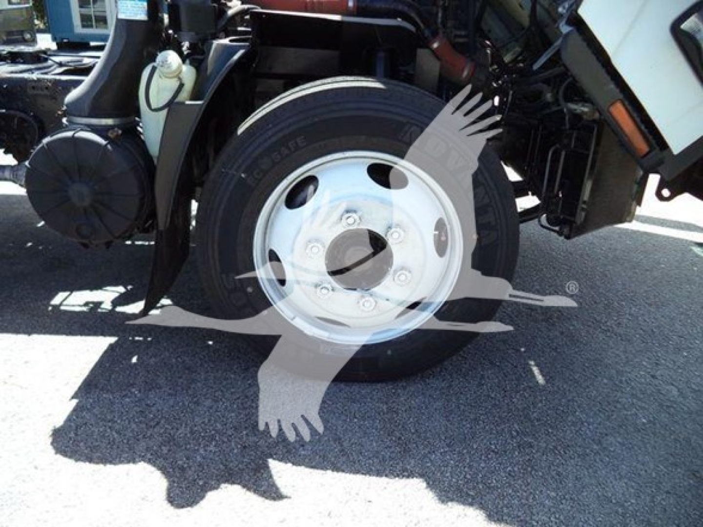 Isuzu NRR front wheel assembly visible with tire and white steel wheel, part of truck chassis and brake components.