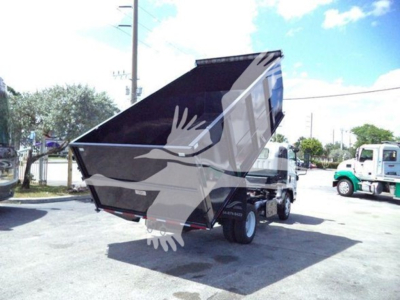 Isuzu NRR dump truck in yard showing dump bed raised with visible rear wheels and chassis.