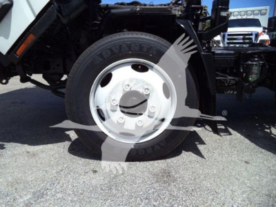 Isuzu NRR truck front wheel and suspension visible; tire shows 'ADVANT' lettering on sidewall; white steel wheel with central hub and lug nuts; bodywork and chassis seen in background.
