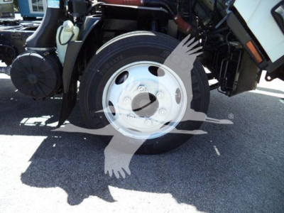 Isuzu NRR front wheel assembly visible with tire and white steel wheel, part of truck chassis and brake components.