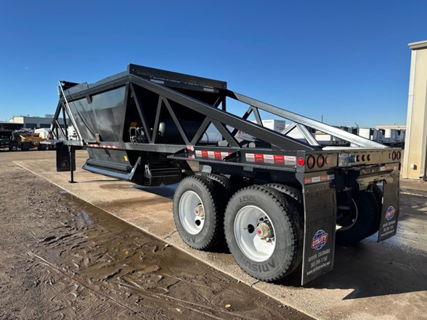 Dump trailer with black frame, dual-axle wheels, lattice side rails, and ramps folded on top showing LW21-40 model plate.