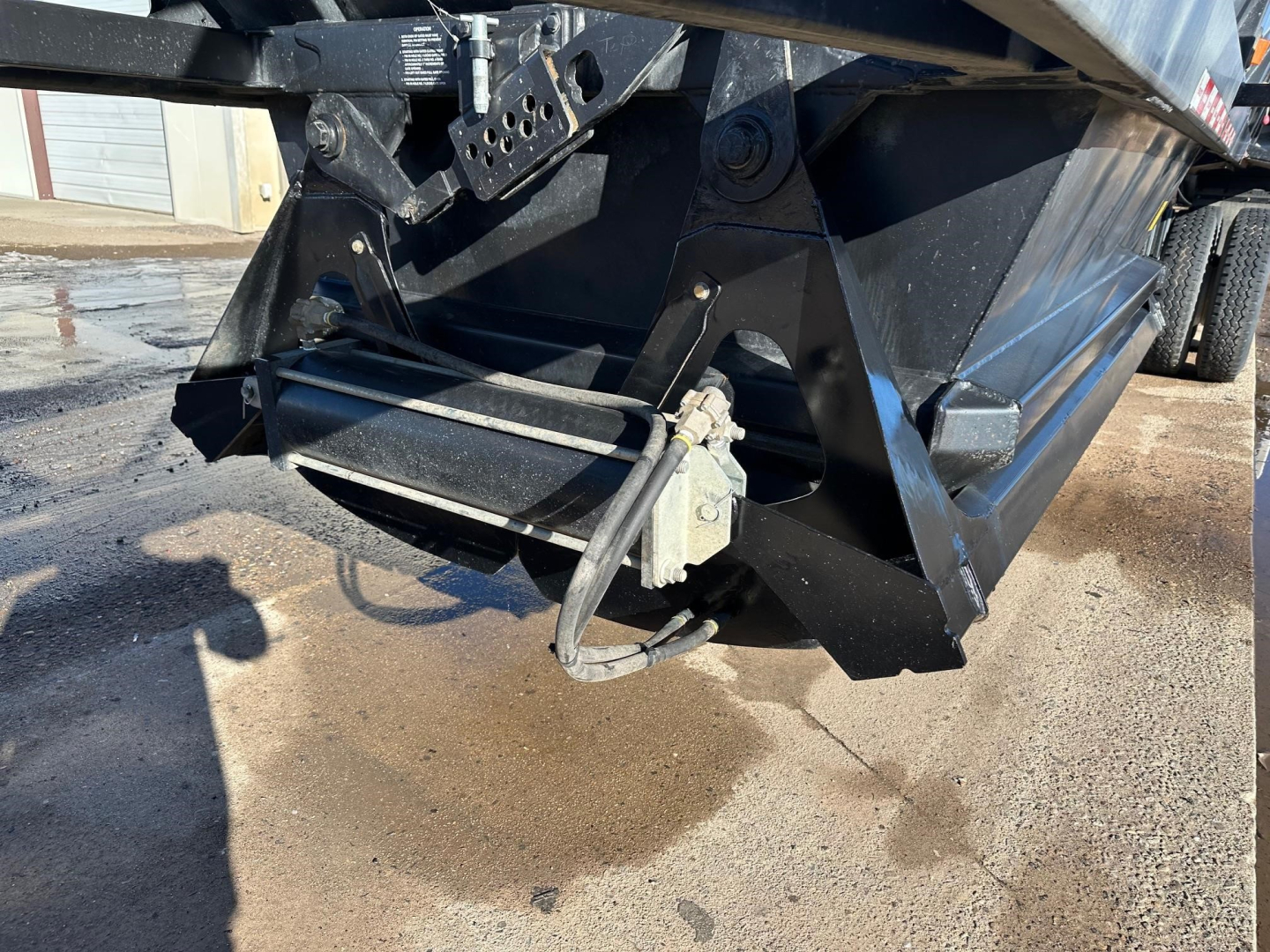 Dump trailer hitch and winch/boot area with hydraulic hoses and mounting brackets visible on black trailer frame.