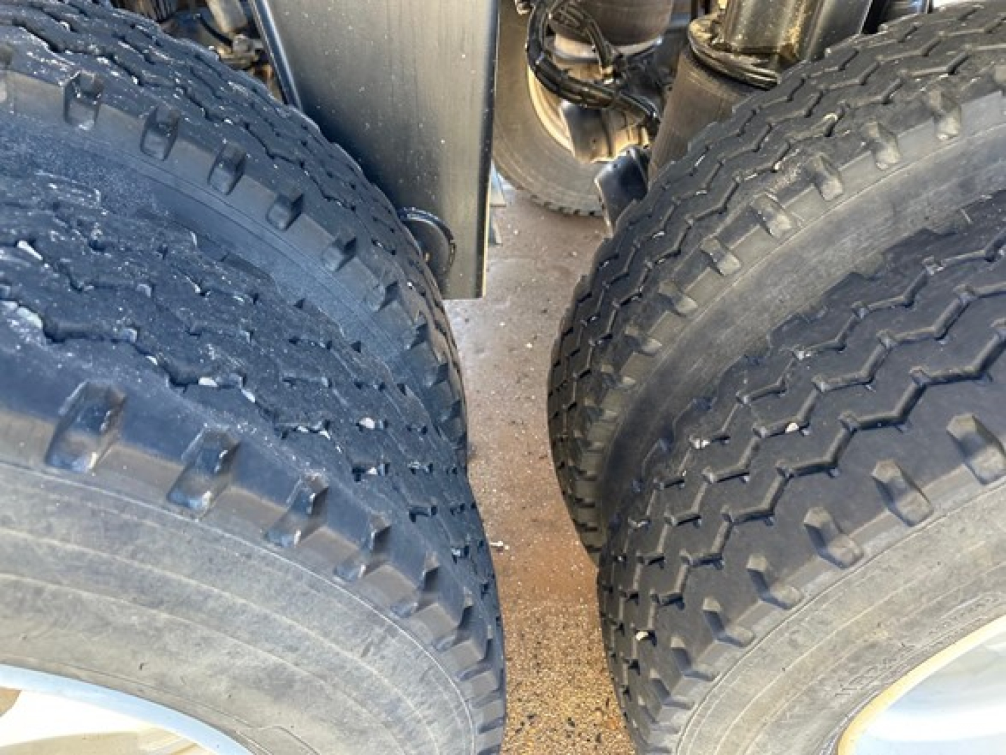 Wheel area of a dump trailer showing dual rear tires with heavy tread and a glimpse of suspension/axle components.