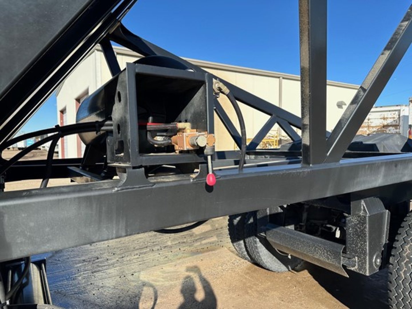 Trailer hitch mechanism on a dump trailer frame with hydraulic pump and metal framework visible.