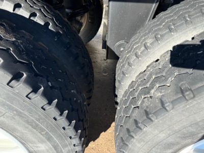 Wheel end of a dump trailer showing dual tires with rugged tread and a glimpse of frame and mudguard.