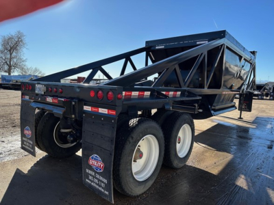 Trailer showing dual rear axles with black truss frame and white wheels, load bed on top, and red tail lights; branding plate and bumper visible.