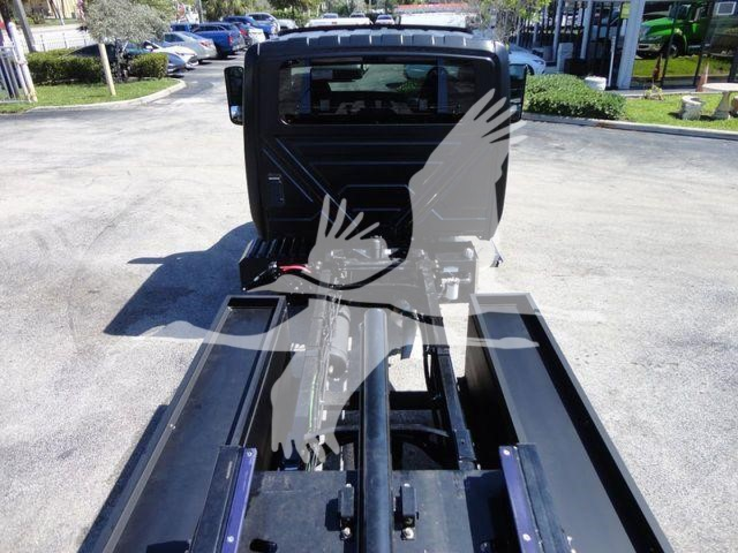 Truck bed view showing chassis and hydraulic system of a rollback truck with cab in background.
