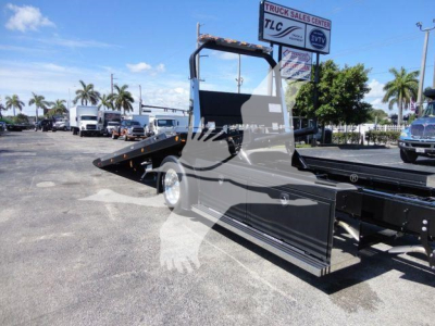 Truck bed and side view of a 2022 International MV rollback truck showing a black steel body, hydraulic ramp, and flatbed with rear wheel visible.