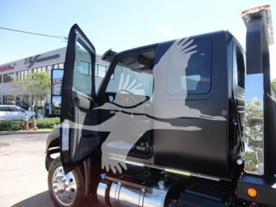 Tractor truck cab with open door showing black exterior and chrome fuel tank, MV International rollback truck, informational decal visible on window.