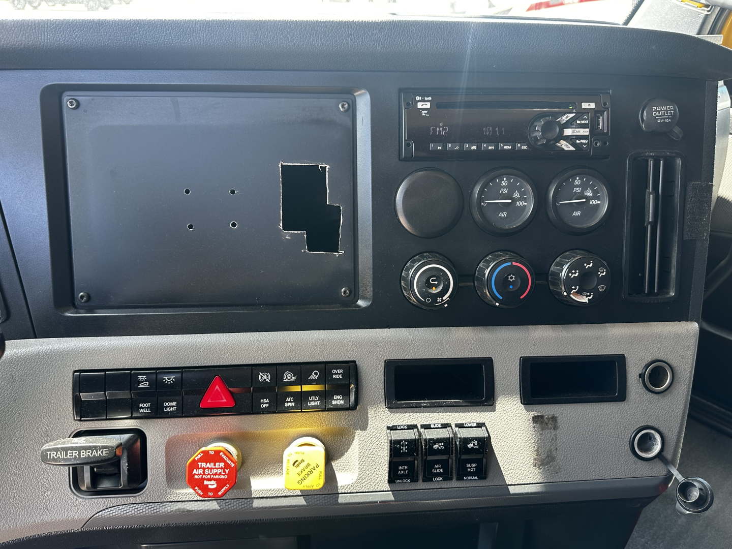 Cab interior front dash of a Freightliner Cascadia 126 truck showing instrument cluster, control panel, empty radio slot, hazard switch, trailer brake control, and assorted switches.