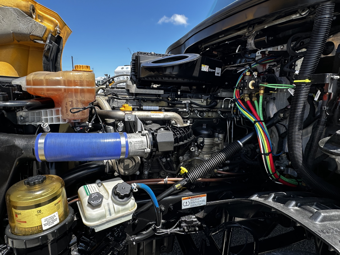 Freightliner Cascadia 126 engine bay view with hoses, wiring, coolant reservoir, and hydraulic fluid reservoir visible