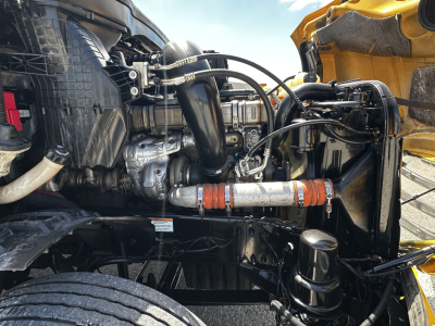 Truck engine bay showing Cummins or Detroit Diesel engine components with hoses and pipes connected to radiator; visible frame and front axle in a Freightliner Cascadia 126.