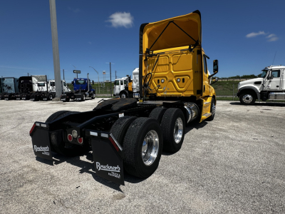 Rear view of a yellow Freightliner Cascadia 126 daycab tractor showing multiple rear axles, mud flaps with Bruckner’s branding, and a clear sky.