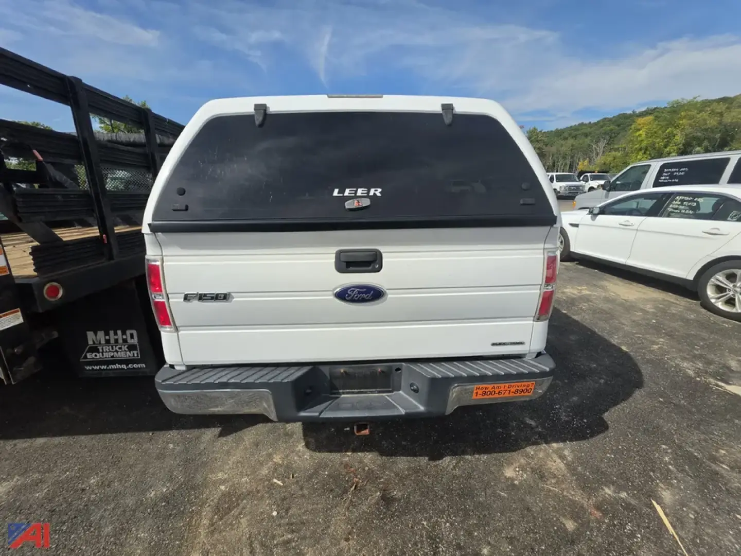 Ford F-150 pickup with Leer camper shell back view showing Ford badge and tailgate, 4x4 crew cab, beige color, license plate area, vehicle dealership lot