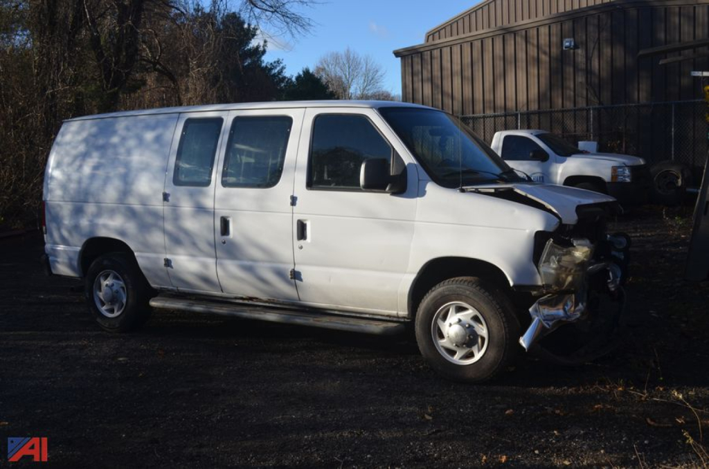 Ford E-350 van side view with front-end damage showing front-right crash impact and missing bumper.