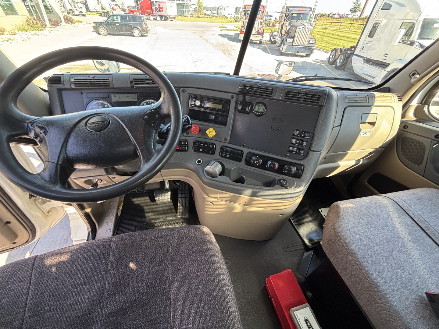 Cab interior of a Freightliner CA12564DC daycab showing steering wheel, instrument cluster, and control panel with various switches.