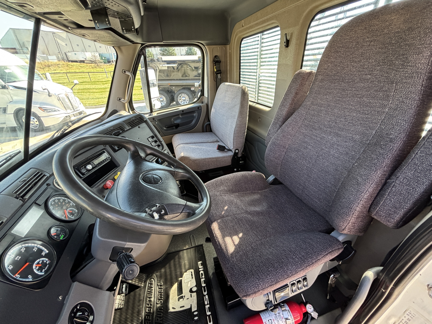 Freightliner CA12564DC cab interior showing steering wheel, dashboard gauges, and two cloth seats.