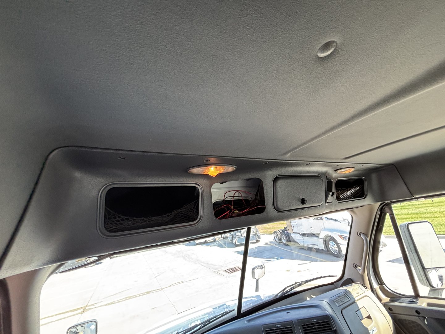 Truck cab interior viewed from passenger side showing overhead storage compartments with wiring and a small light fixture