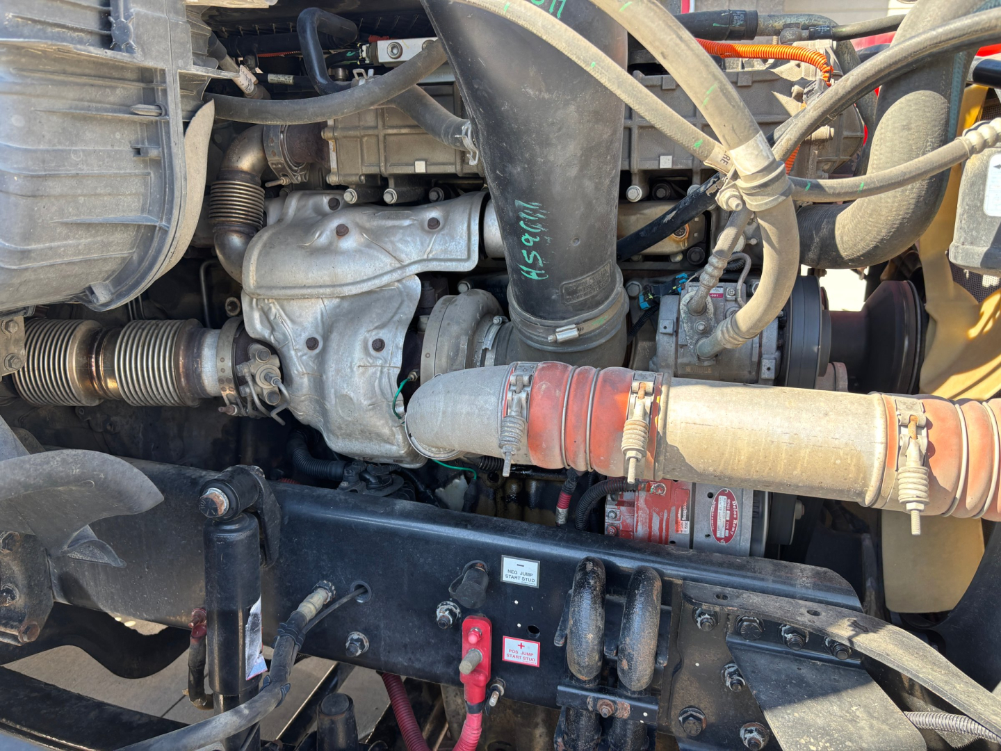Engine bay view of a 2017 Freightliner CA12564DC showing hoses, tubes, and engine components with a red coupler and black chassis crossmember.