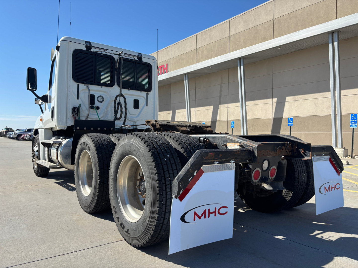 Truck cab and rear chassis of a Freightliner CA12564DC with dual rear axles and white mud flaps, license-free yard setting.