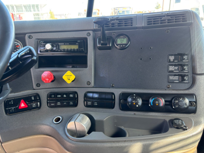 Cab interior of a Freightliner CA12564DC daycab showing dashboard controls, radio, hazard button, ignition, and climate controls.