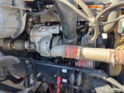 Engine bay view of a 2017 Freightliner CA12564DC showing hoses, tubes, and engine components with a red coupler and black chassis crossmember.
