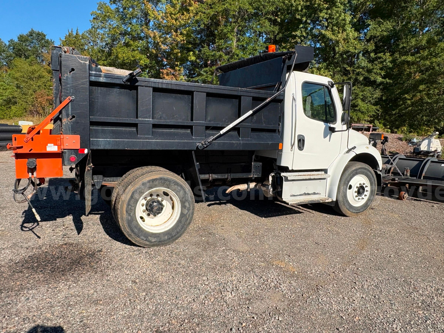 Dump truck side view showing Freightliner M2 dump bed with white cab and black bed.