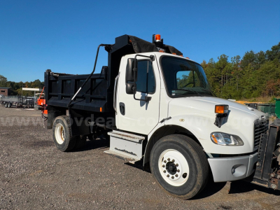 Dump truck in-service 2015 Freightliner M2 with white cab and black dump bed, front-right view.