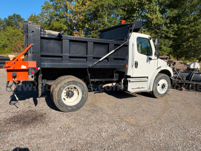 Dump truck side view showing Freightliner M2 dump bed with white cab and black bed.