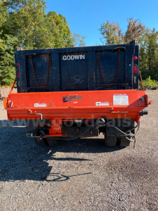 Rear view of a 2015 Freightliner M2 dump truck with an orange Swenson dump body. Visible text includes GODWIN on the black tailgate, SWENSON/SWENSON logo on orange frame, warning labels and wiring harness near the hitch.