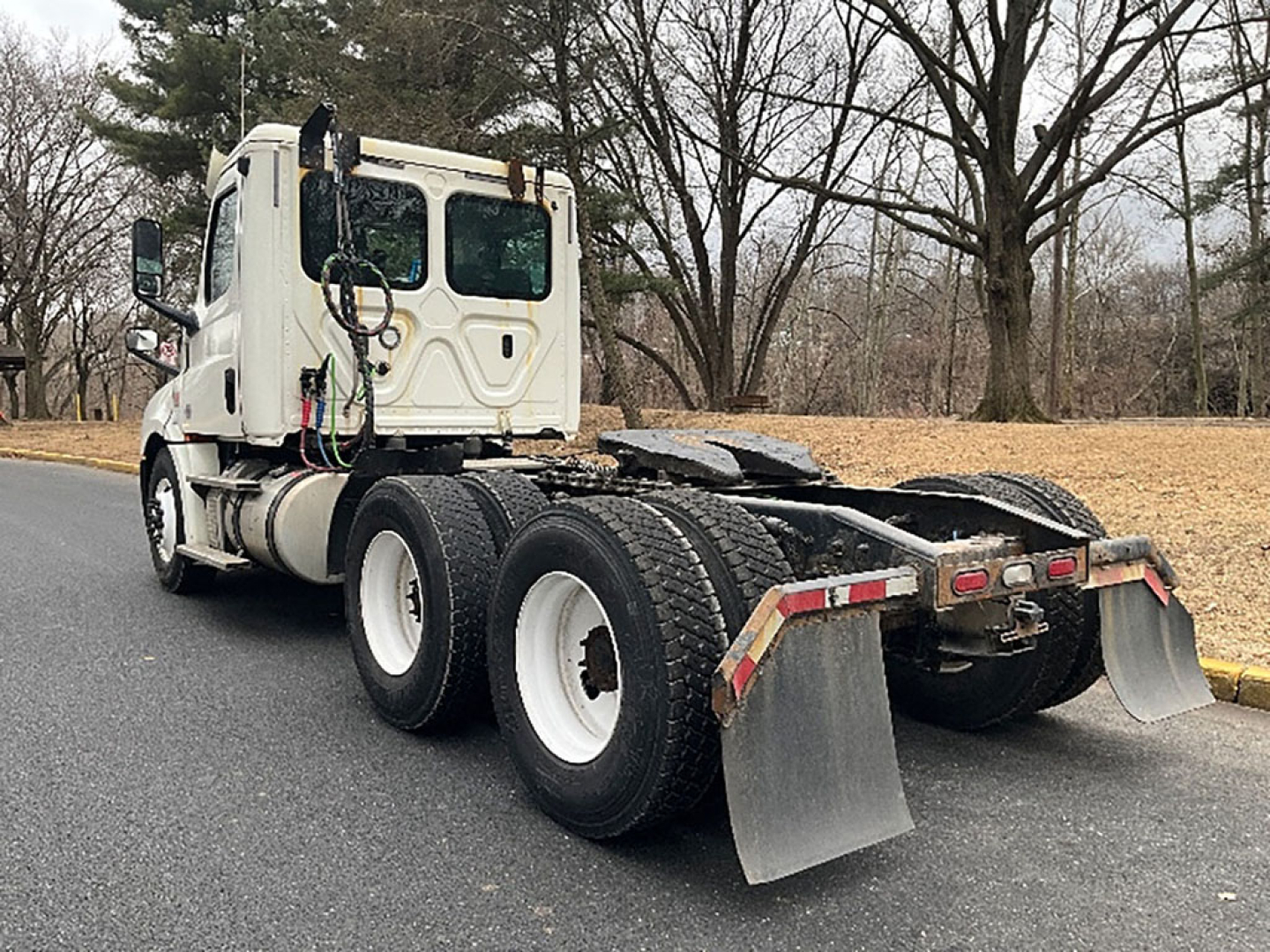 Wheel-lift Freightliner Cascadia daycab tractor from rear three-quarter view showing tandem axles and mud flaps.
