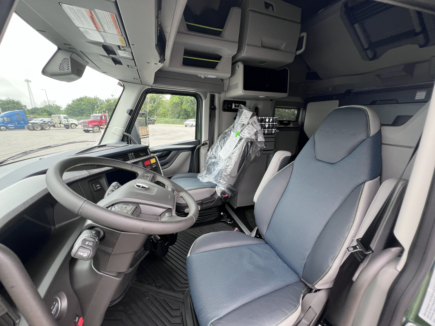Volvo VNL64T860 cab interior showing steering wheel, driver's seat, overhead storage compartments, and wrapped seat cover.